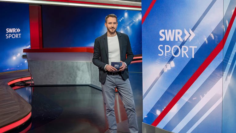 SWR Sport Moderator Benjamin Wüst in der SWR Sport Studiodekoration mit dem SchriftzugLogo SWR Sport