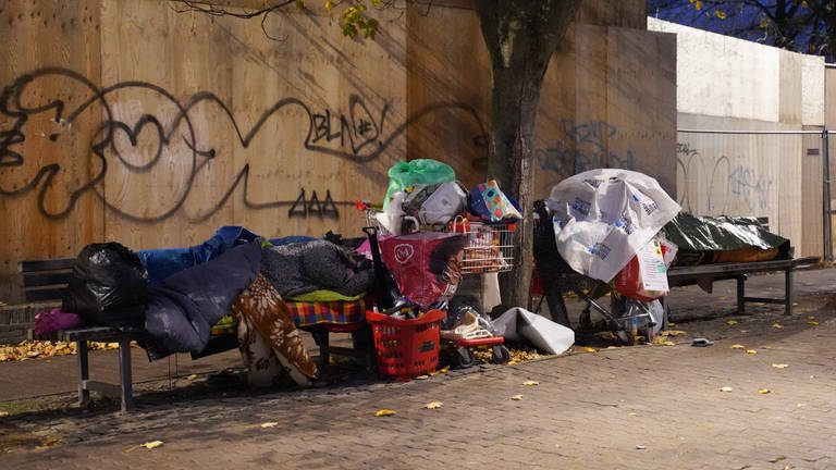 Zwei obdachlose Mesnchen schlafen umgeben von ihrem Hab und Gut auf Bänken unter einer Brücke