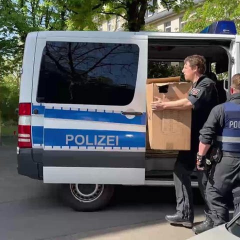 Polizisten tragen Kartons mit Beweismaterial aus dem Auto in ein Gebäude