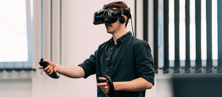 Sebastian Demuth beim Testen eines digitalen Produktes des SWR X Lab, er ist mit einem VR-Headset und zwei Controllern ausgestattet.