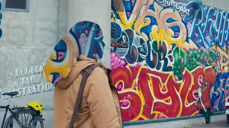 Frau läuft an einem Graffiti vorbei. Sie ist anonymisiert.