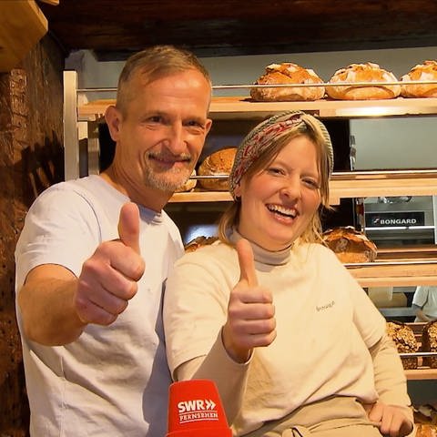 Hausarzt Jörn und seine Tochter Nora stehen lachend vor der Auslage, in der frische Brote liegen, in ihrer Konstanzer Bäckerei. Sie machen beide einen Daumen nach oben. 
