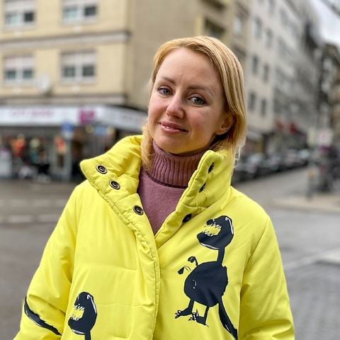 Kateryna aus der Ukraine steht in Innenstadt von Pforzheim. Sie trägt einen schrillen gelben Mantel und schaut in die Kamera.  (Foto: SWR)