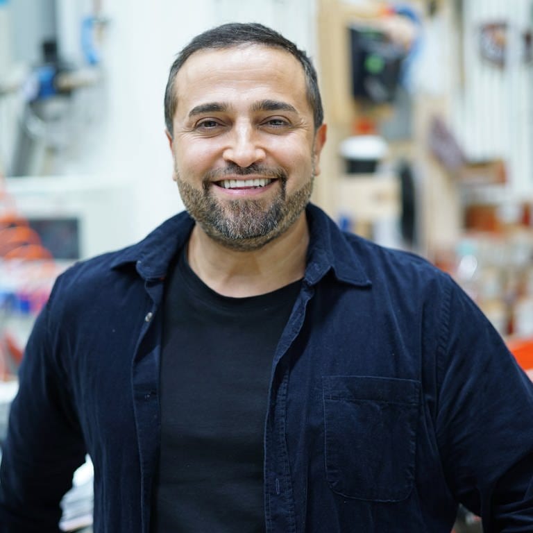 Ehemann Murat Özcan von Sallys Welt steht in einer Werkstatt und schaut lächelnd in die Kamera. (Foto: SWR)