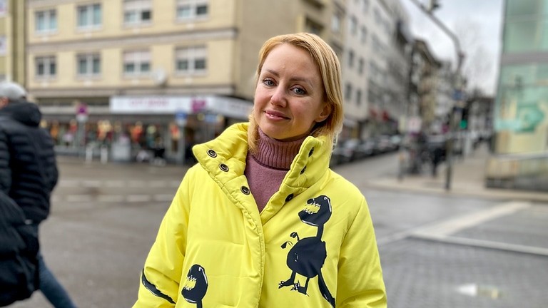 Kateryna aus der Ukraine steht in Innenstadt von Pforzheim. Sie trägt einen schrillen gelben Mantel und schaut in die Kamera.  (Foto: SWR)