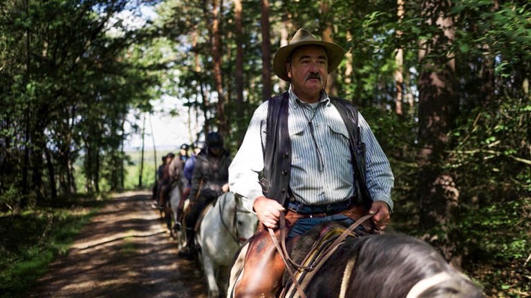 Mann mit Cowboyhut und Schnurrbart sitzt auf Pferd, hinter ihm andere Reiter. (Foto: SWR)