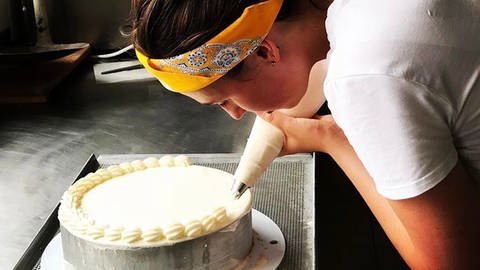 Eine junge Frau arbeitet in einer Konditorei an einer Torte.  (Foto: SWR)