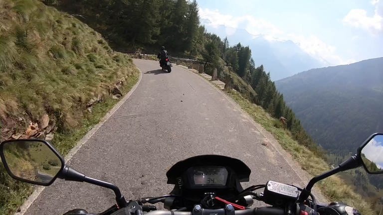 Bild aus Sicht eines Motorradfahrers, der durch eine Landschaft von hohen Bergen fährt.