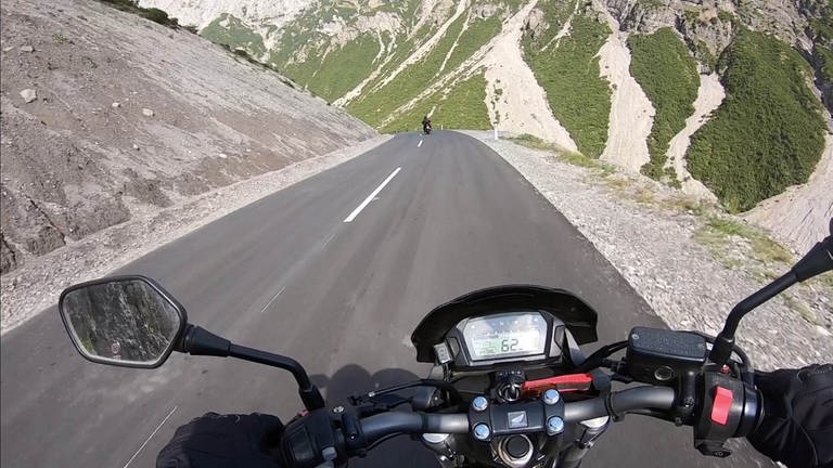 Bild aus Sicht eines Motorradfahrers, der durch eine Landschaft von hohen Bergen fährt. 