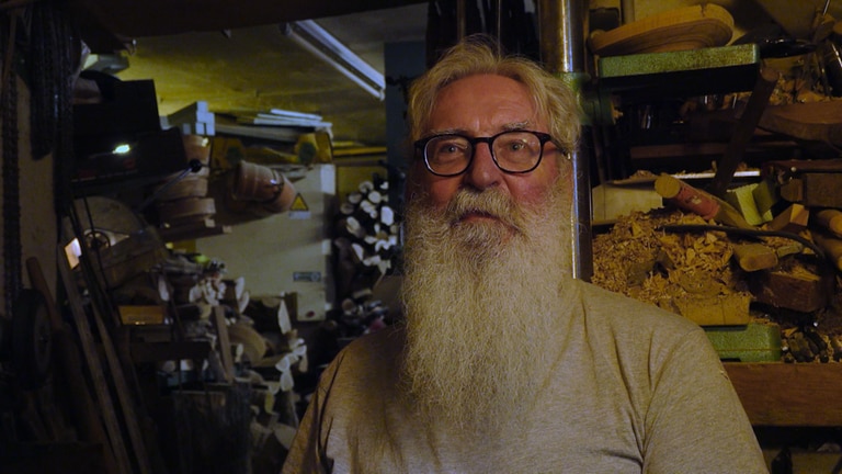 Ein älterer Mann mit Brille und langem weißen Bart steht vor Holzregalen in einem Schuppen (Foto: SWR)