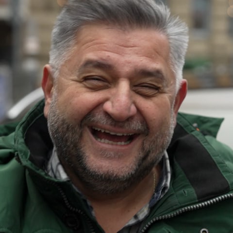 Iraklis ist Taxifahrer in Stuttgart. Er steht in der Stadt und lächelt herzlich in die Kamera.  (Foto: SWR)