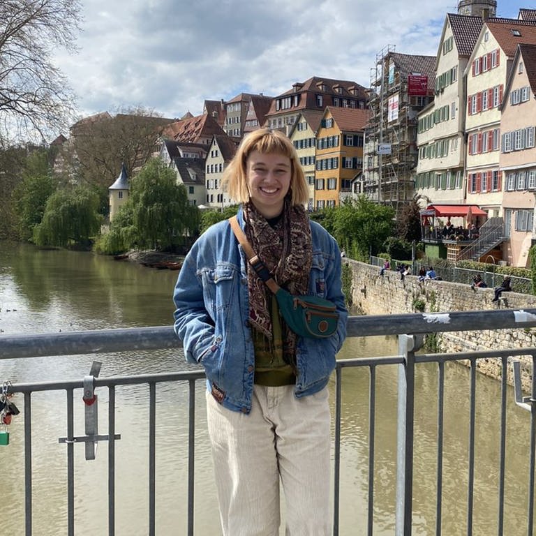 Laura steht auf der Eberhardsbrücke in Tübingen. Sie hat eine Jeansjacke an und ihre Hände in den Taschen. Hinter ihr sieht man Tübingen mit dem Hölderlinturm.  (Foto: SWR)