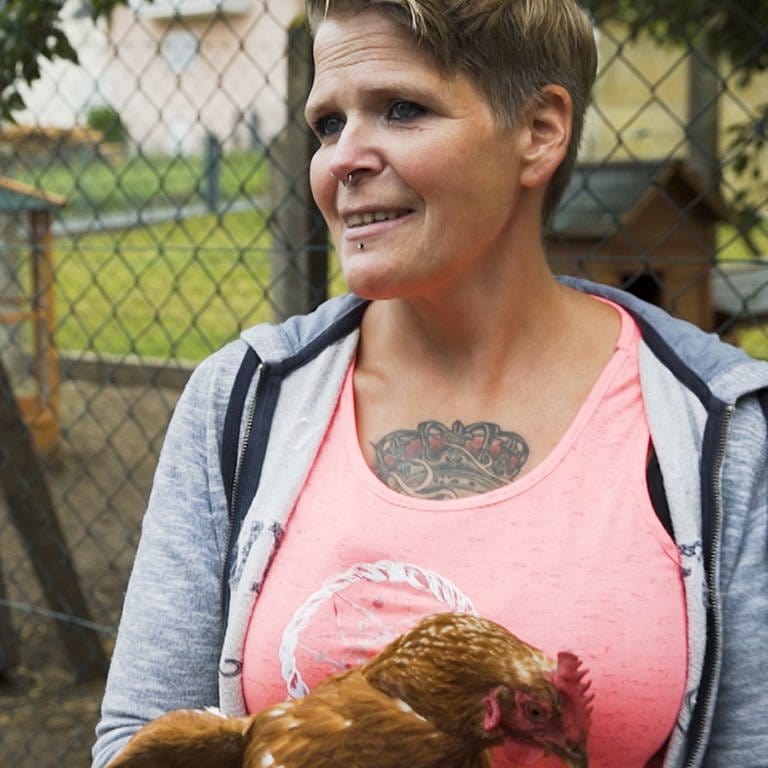 Frau mit Huhn im Arm im Freiluftgehege