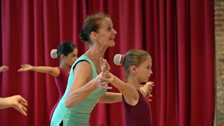Die Ballettlehrerin korrigiert die Bewegungen der Kinder beim Training in der Tanzschule.