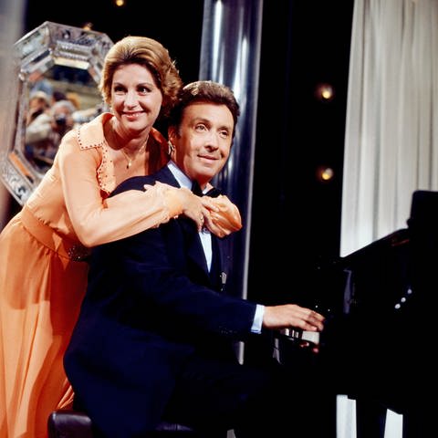 Sängerin Johanna von Koczian umarmt den Entertainer Peter Alexander von hinten, während er am Klavier sitzt. Das Bild stammt aus einer Fernsehsendung aus dem Jahr 1977. (Foto: picture-alliance / Reportdienste, United Archives)