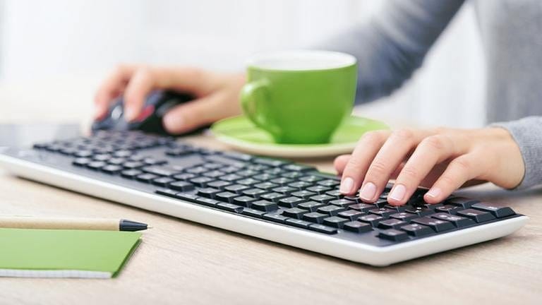 Eine Frau sitzt vor ihrem Computer und einer grünen Tasse und tippt in ihre Tastatur (Foto: Colourbox)