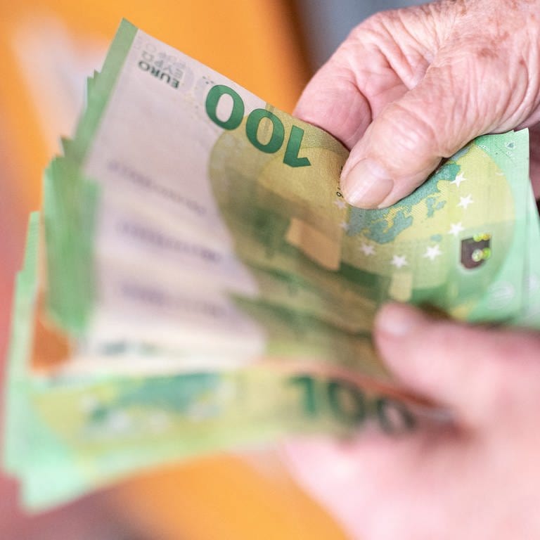 Die Hände einer älteren Frau halten 100-Euro-Scheine aufgefächert hin.  (Foto: dpa Bildfunk, Picture Alliance)