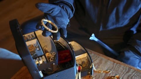 Einbruch – was tun? Ein Einbrecher mit Handschuhen plündert eine Schmuckschatulle. (Foto: IMAGO, Jochen Tack)
