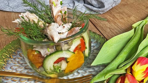 bunter Salat mit Räucherfisch im Glas auf einem grünen Teller mit Gabel, daneben Tulpen 