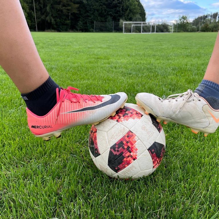 Die Füße zweier Fußballspielerinnen auf einem Ball.