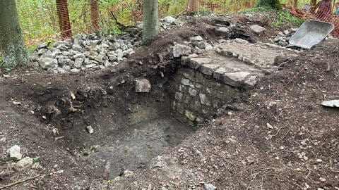 Mit roten Netzen abgesperrter Bereich, in dessen Mitte ein Loch bis zum Felsgrund geht. Daran erkennt man den Ausschnitt einer steinernen Mauer der Burg auf dem Schlössleberg.