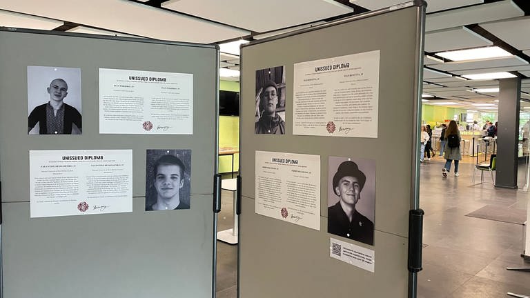 Eine Stellwand mit vier Porträts von jungen Männern in der Ausstellung "Unissued Diplomas". Sie zeigt in der Universitätsbibliothek Fotos von jungen Menschen, die im Krieg in der Ukraine gestorben sind.