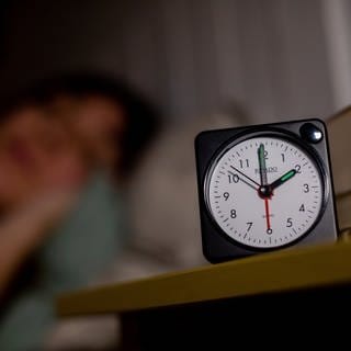 Eine Frau schläft neben einem Wecker, welcher auf 2 Uhr zeigt. Am 31.10.2021 endet die Sommerzeit (MESZ), es ist wieder mitteleuropäische Normalzeit, die umgangssprachlich auch Winterzeit genannt wird. In der Nacht zum 31. Oktober wird in Deutschland die Uhr um 3 Uhr auf 2 Uhr zurückgestellt.  (Foto: dpa Bildfunk, Picture Alliance)