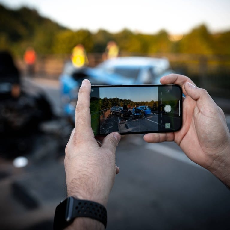 Ein Gaffer macht mit seinem Smartphone Bilder von einer Unfallstelle. In Mainz wurden nach einem tödlichen Unfall Bilder und Videos von einem der Opfer gemacht und ins Netz gesetellt. Die Polizei ermittelt.