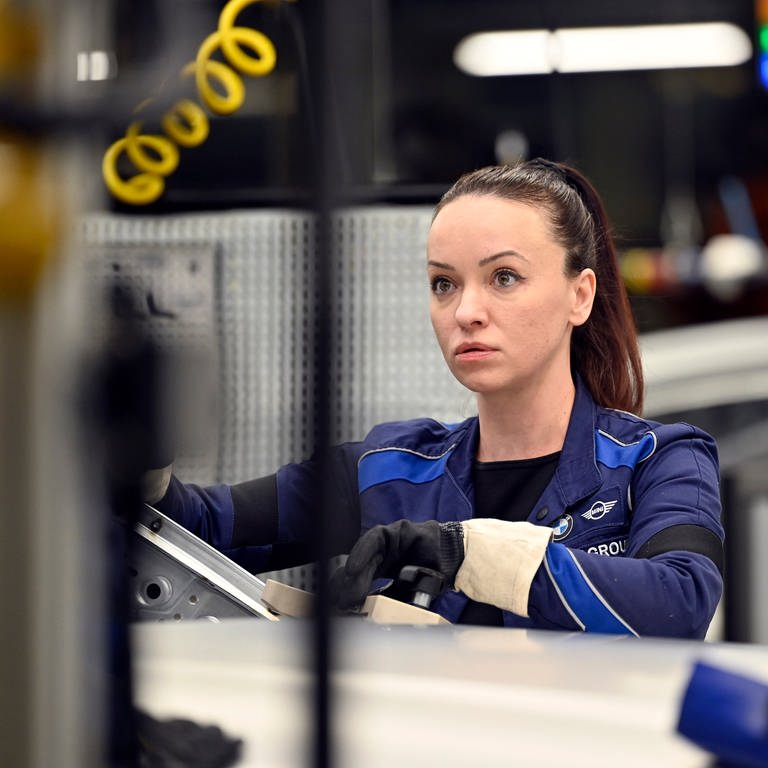 Fachkräftegewinnung geglückt: Eine junge Frau steht in der Werkhalle eines Autobauers an einer Maschine 