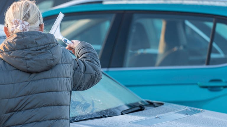 Das Wetter bleibt kalt: Eine ältere Frau kratzt in RLP mit einem Eiskratzer die Windschutzscheibe ihres Auto frei. Der April-Winter hat Rheinland-Pfalz weiter im Griff. (Foto: dpa Bildfunk, picture alliance / CHROMORANGE | Michael Bihlmayer)
