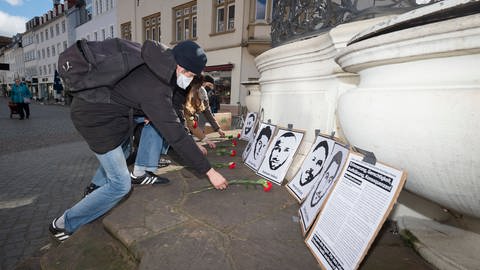 Mehrere Personen legen an  den Portraits der Ermordeten von Hanau rote Nelken nieder. 