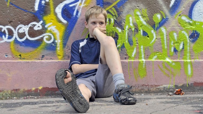 Lustloser neunjähriger Junge sitzt am Boden auf einem Bolzplatz (Foto: IMAGO, imagebroker)