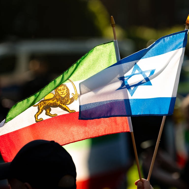 Ein Mann hält eine israelische (r) und eine iranische Fahne