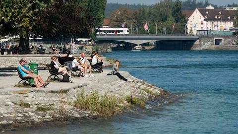 Menschen sitzen bei Sonnenschein am letzten Tag der Sommerferien in Baden-Württemberg an der Promenade.
