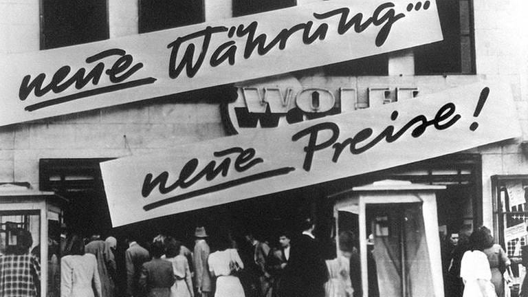 Kundenandrang vor einem Geschäft, das nach der Währungsreform 1948 Schilder mit der Aufschrift "Neue Währung... neue Preise!" an der Hausfassade angebracht hat.