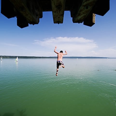 Ein Mann springt von einem Sprungturm ins kühle Wasser