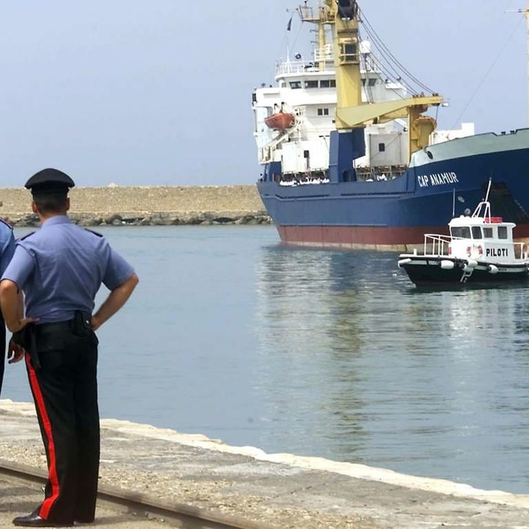 Italienische Polizisten schauen am 12. Juli 2004 auf das deutsche Rettungsschiff "Cap Anamur" beim Anlegen im sizilianischen Hafen Porto Empedocle