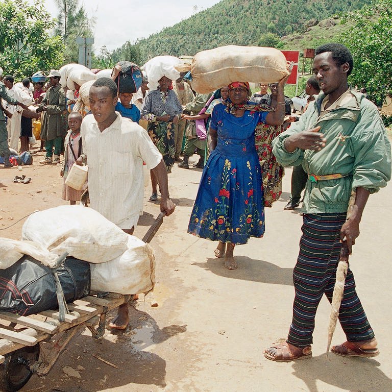 12. April 1994: Angehörige der Hutu fliehen südlich von Kigali vor den schweren Kämpfen zwischen den Regierungstruppen der Hutu und den Rebellen der Rwanda Patriotic Front (RPF) der Tutsi. Der Mann rechts ist Zivilist, Hutu und arbeitet auf der Seite der Regierungstruppen. Er kontrolliert die Flüchtlinge um sicherzustellen, dass keine Tutsi darunter sind. Hunderttausende Menschen fliehen nach dem Mord am Präsidenten Ruandas am 6. April 1994 vor den Massakern in Kagali und Umgebung.  (Foto: picture-alliance / Reportdienste, picture alliance / ASSOCIATED PRESS | Jean-March Bouju)