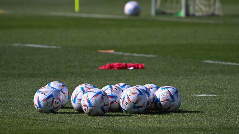 Fußbälle mit der Aufschrift: "FIFA World Cup Qatar 2022" liegen beim Training auf dem Rasen.