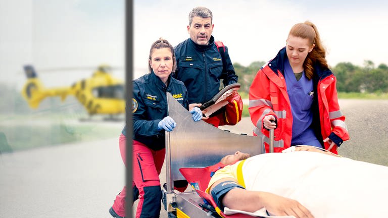 Ein Rettungsteam bringt einen Verletzten in die Unfallklinik, der Rettungshubschrauber Christoph 5 im Hintergrund
