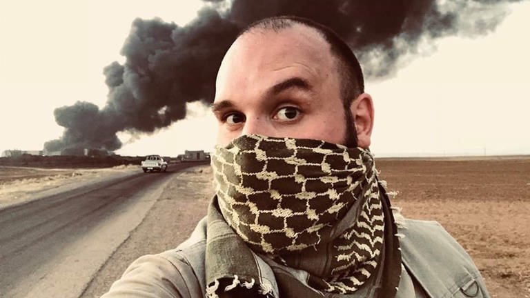 Konstantin Flemig vor einer Erdölraffiniere in den kurdischen Gebieten Syriens. Zum Schutz vor Rauch hat er einen Schal vor Mund und Nase.