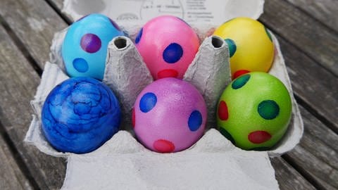 Bunte Eier aus dem Supermarkt sollten gekühlt gelagert werden.  Das Bild zeigt bemalte Ostereier in einem Eierkarton. Symbolbild.