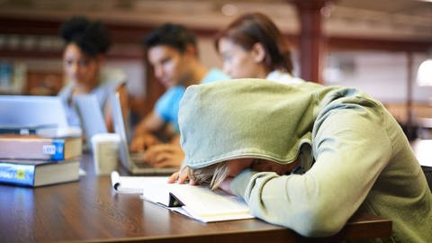 Ein Junge schläft in der Schule mit dem Kopf auf den Tisch gelegt, tags: innere Uhr, Bildschirmnutzung, Schlafenszeit