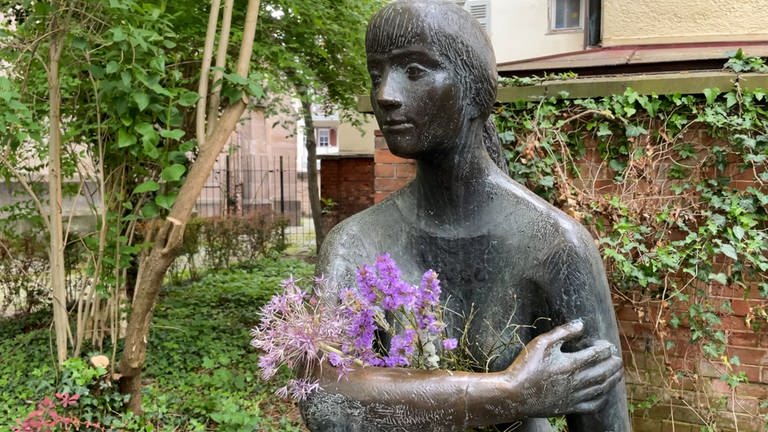 Man sieht eine Skulptur. In Tübingen nennt man sie: die "Sitzende". Ihr werden immer wieder Blumen in die Arme gelegt. Heute hat sie nur einen kleinen Strauss. (Foto: SWR)