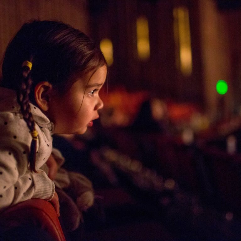 Ein Mädchen lehnt sich im Theatersaal neugierig über die Lehne