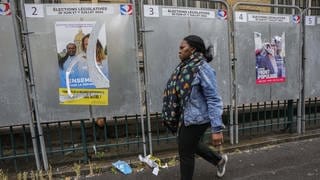 Eine Frau geht in Paris an einer Wand mit abgerissenen Wahlplakaten vorbei