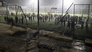 Anwohner stehen auf einem Fußballplatz auf den Golanhöhen, in das eine Rakete eingeschlagen ist.