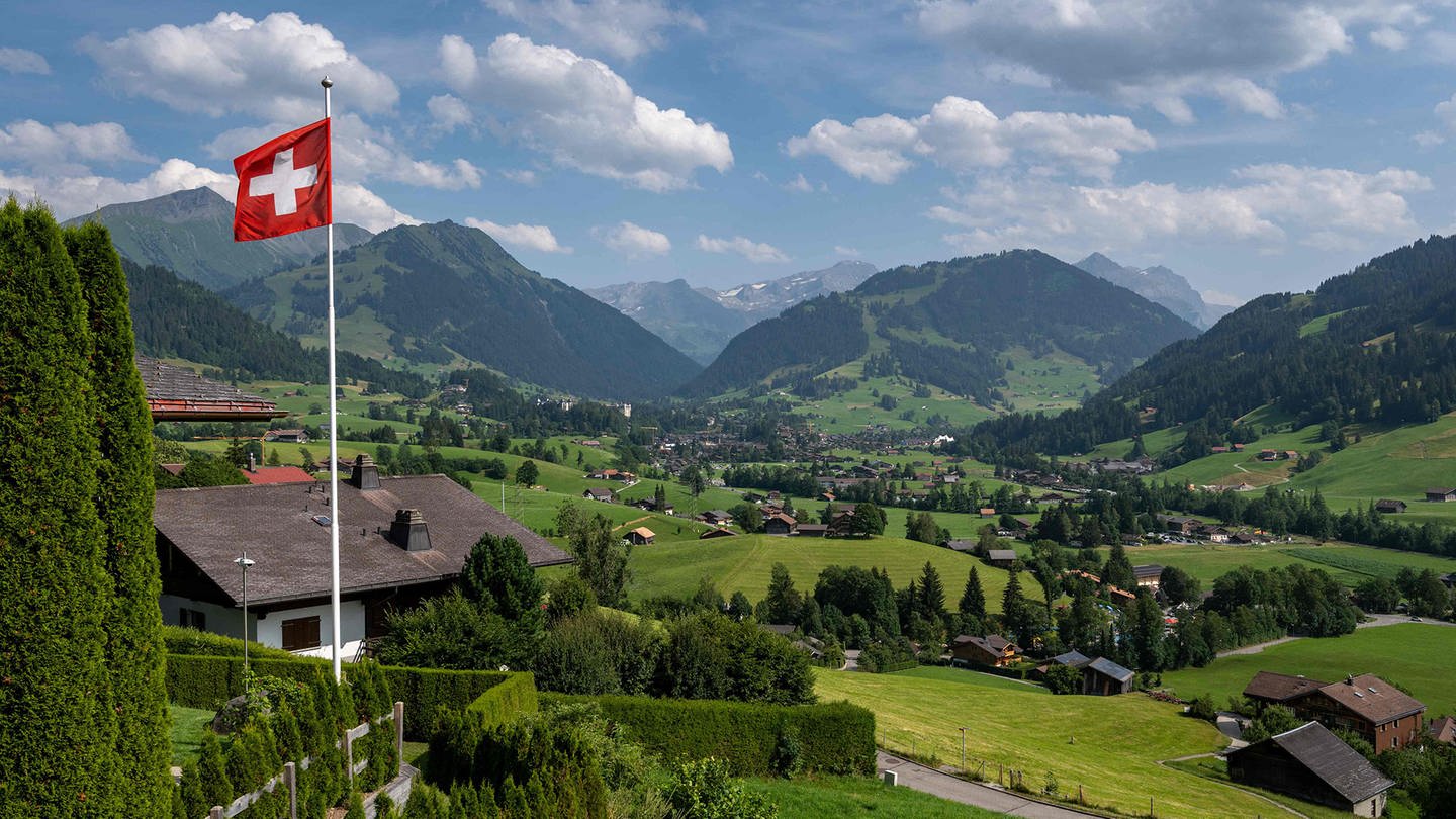 Die Flagge der Schweiz an einem Fahnenmast vor den Alpen.