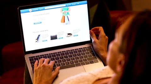 Eine Person auf einem Sofa mit einem Laptop beim Onlineshopping.