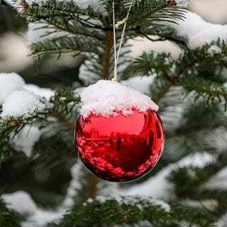 Schnee bedeckt einen Weihnachtsbaum und den Baumschmuck.